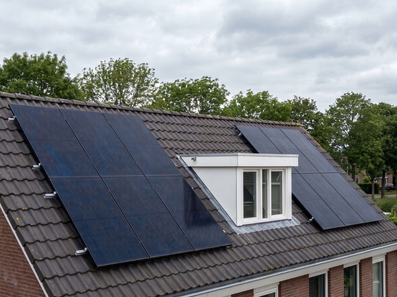 Zonnepanelen op een pannendak naast een witte dakkapel